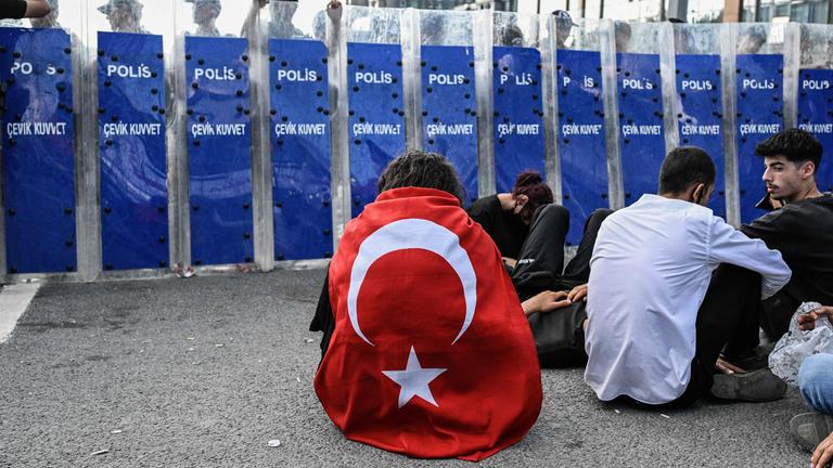 Ein Demonstrant trägt sitzend vor einer Polizeiblockade in Istanbul eine türkische Flagge um den Rücken gebunden.
