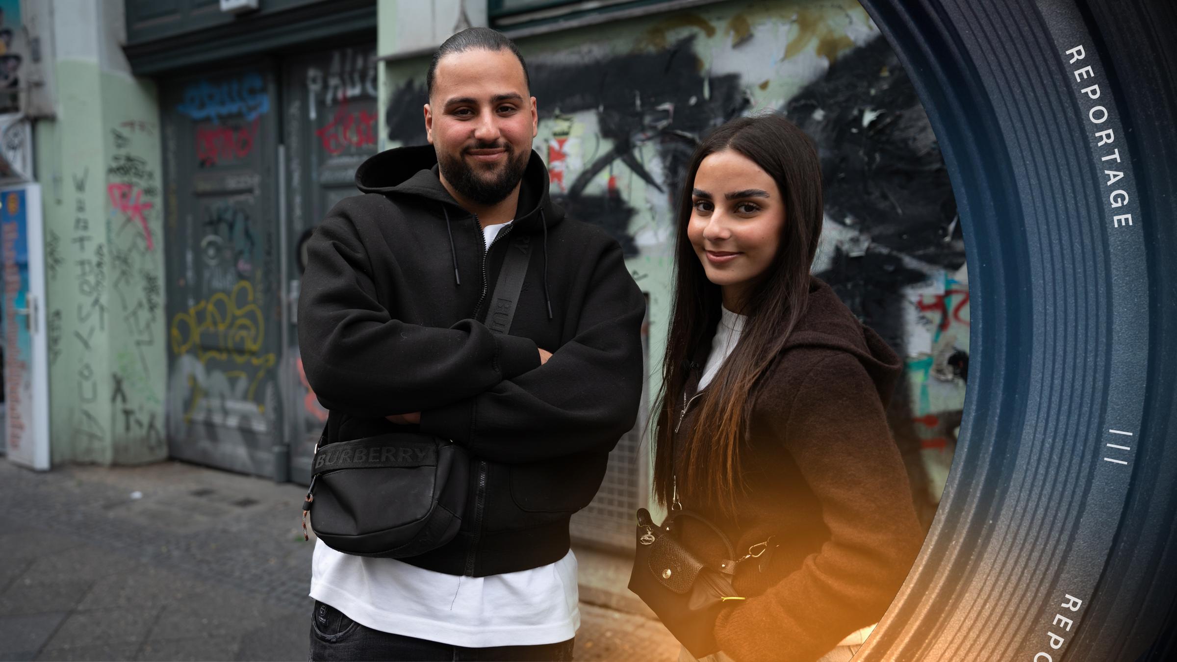 Melih Saydam und seine Schwester Melike stehen auf einer Straße in Berlin. Im Hintergrund ist eine Hauswand mit Graffiti.
