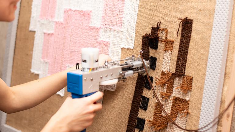 Mit einer Tufting-Pistole wird ein Teppich in einem Rahmen angefertigt.