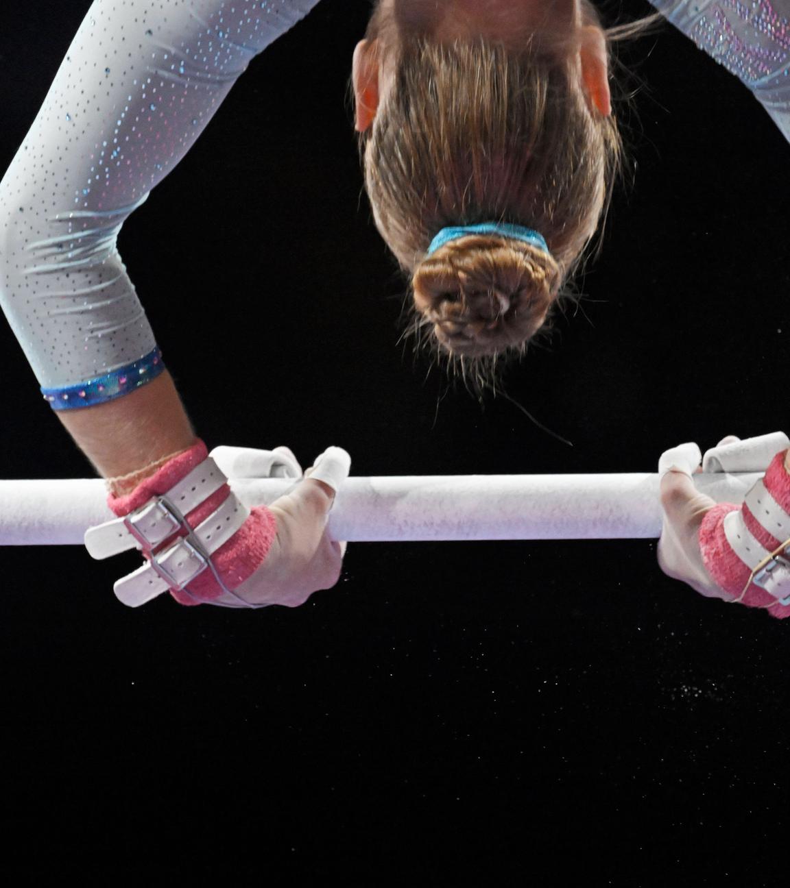 Nachaufnahme der Hände und der Kopfes einer Turnerin, die kopfüber über eine Heckstange schwingt.