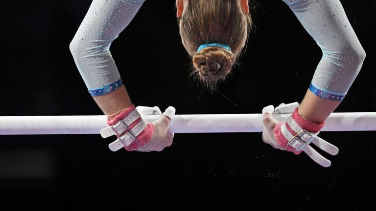 Nachaufnahme der Hände und der Kopfes einer Turnerin, die kopfüber über eine Heckstange schwingt.