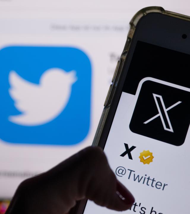 Auf dem Profil von Twitter auf dem Smartphonebildschirm ist der weiße Buchstabe X auf schwarzem Hintergrund zu sehen, während im Hintergrund das bisherige Logo von Twitter angezeigt wird.
