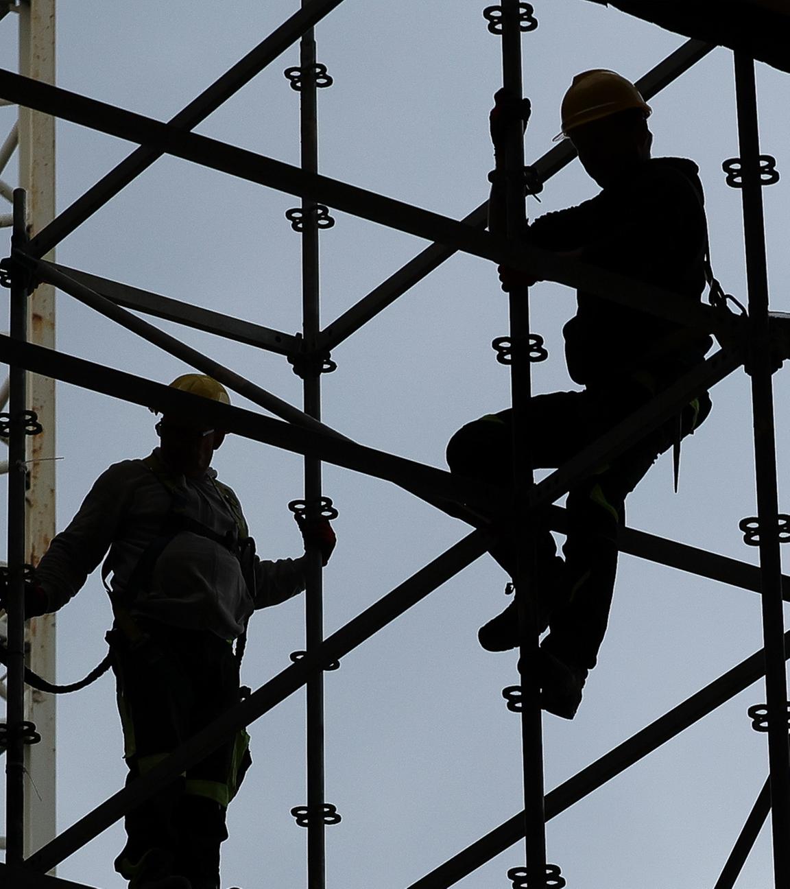 Sillhuette von Gerüstbauern die mit einem Gurt gesichert auf einer Baustelle arbeiten.