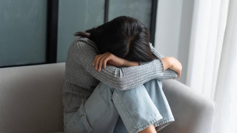Junge Frau sitzt traurig auf dem Sofa. (Symbolbild)