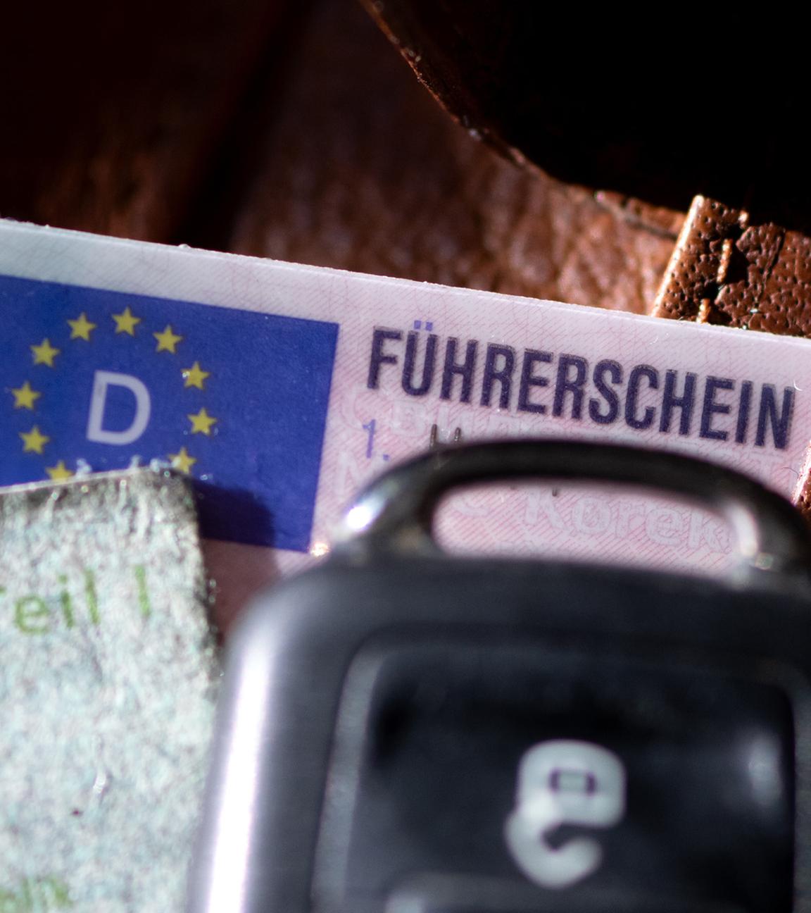 Ein Führerschein, ein Autoschlüssel und eine Zulassungsbescheinigung liegen auf einem Portemonnaie.