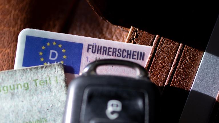 Ein Führerschein, ein Autoschlüssel und eine Zulassungsbescheinigung liegen auf einem Portemonnaie.