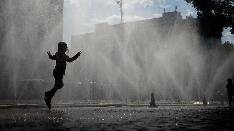 Passanten erfrischen sich an Wasserfontänen, die von der Stadt Köln im Rahmen der Hitzeaktion 'Cooling Cologne' auf dem Rudolfplatz ausgelegt wurden.