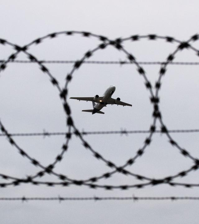 Ein Flugzeug startet - fotografiert durch Stacheldraht am Flughafenzaun. (Symbolbild)