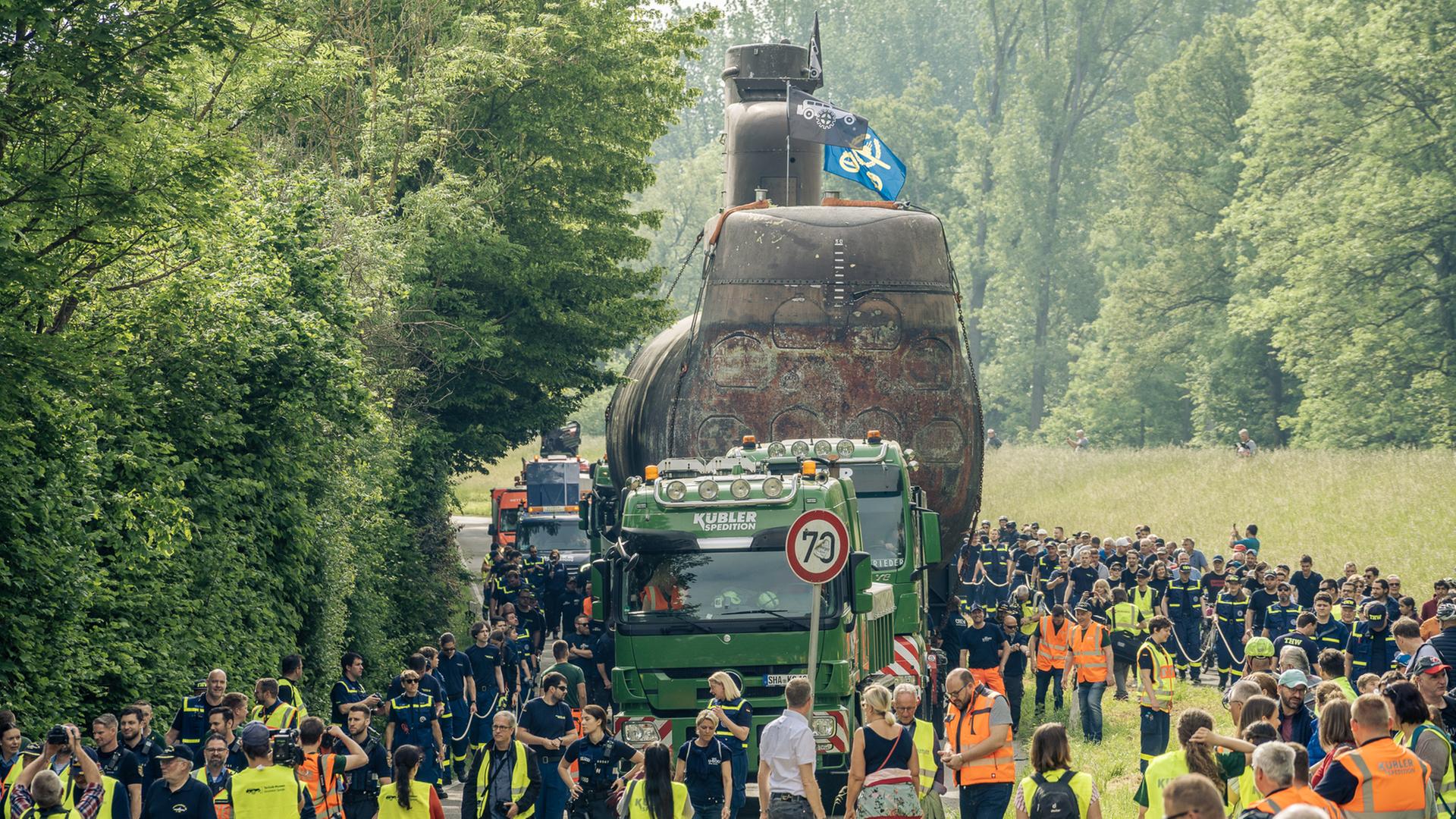 Das U-Boot wird auf einem Lkw transportiert, umringt von vielen Menschen