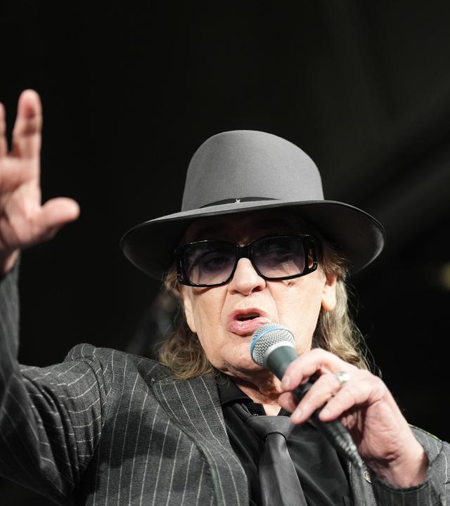 Udo Lindenberg mit Hut und Sonnenbrille, wie er in ein Mikrofon spricht