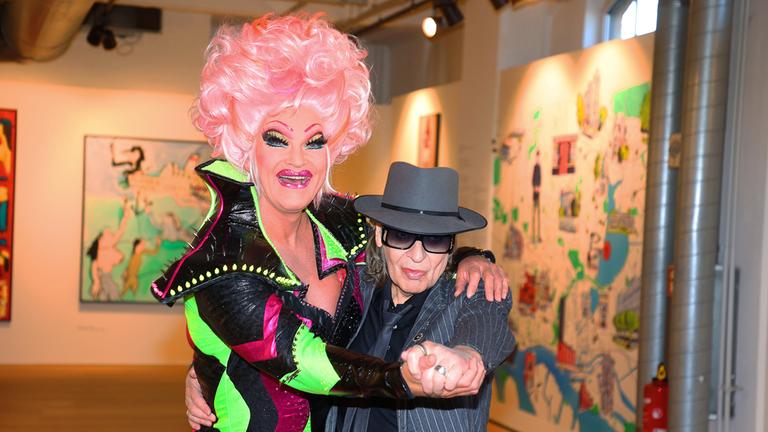 Olivia Jones und Udo Lindenberg sind zu sehen. Jones legt die Arme um Lindenberg und beide lächeln in die Kamera.