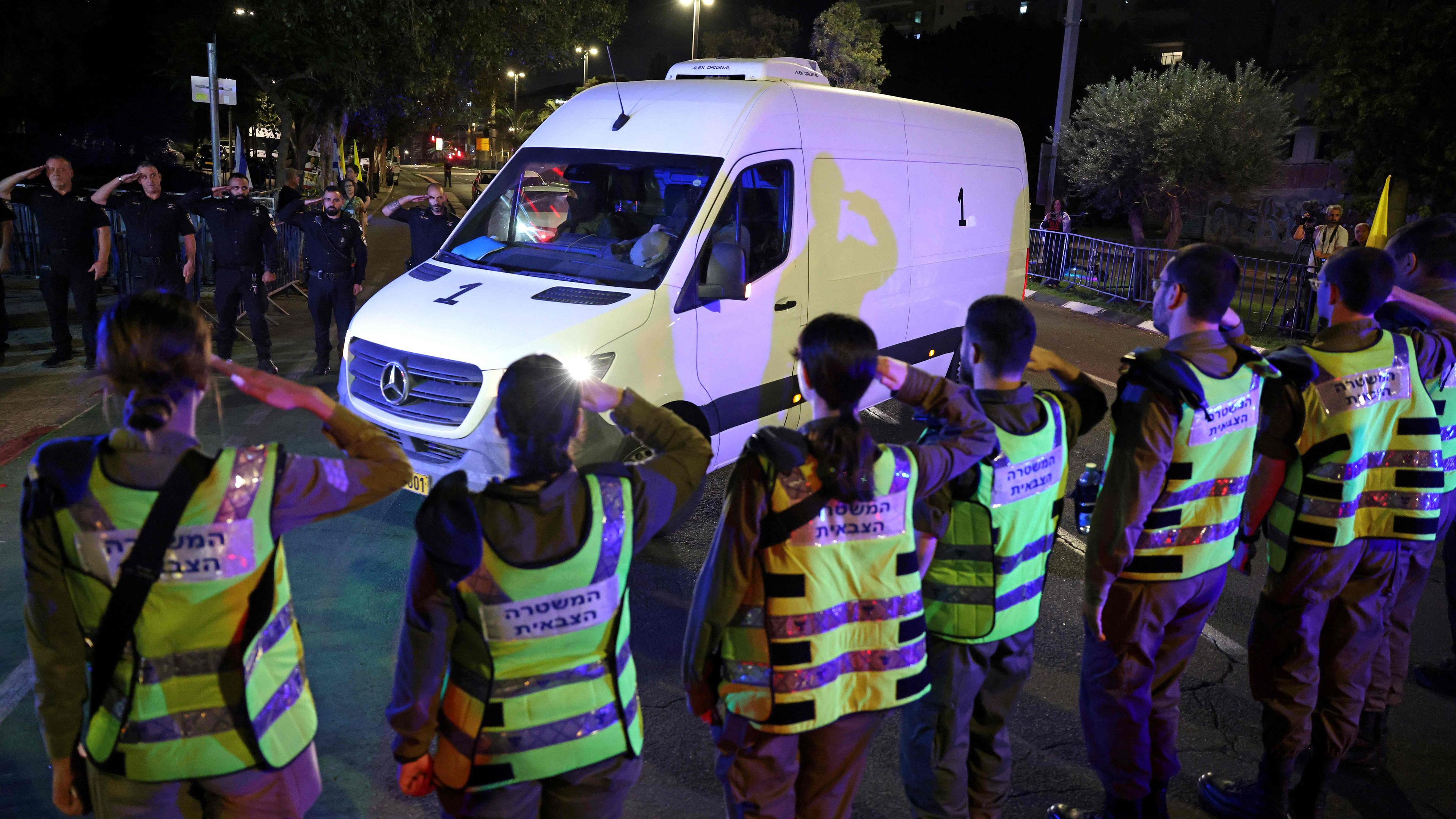 Sechs Menschen in Warnwesten salutieren vor einem weißen Transporter, die die Leichen von vier israelischen Geiseln transportiert.