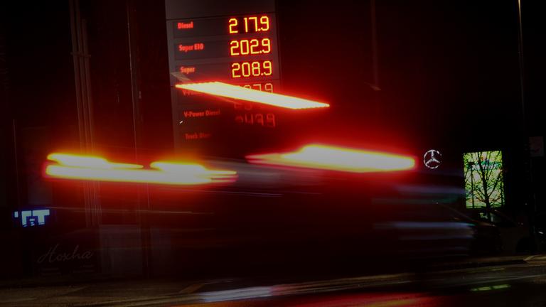 Autos fahren am frühen Morgen im Regen an der Anzeigetafel einer Tankstelle vorbei auf der Benzin- und Dieselpreise zu sehen sind.