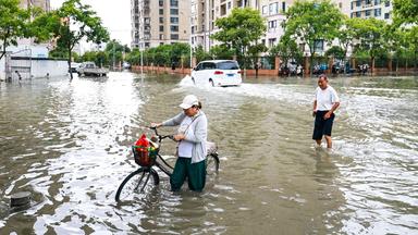 Anwohner versuchen am 12.07.2026 in der Stadt Yueqing, in der ostchinesischen Provinz Zhejiang, eine überflutete Straße nach dem Taifun "Bavi" zu überqueren.