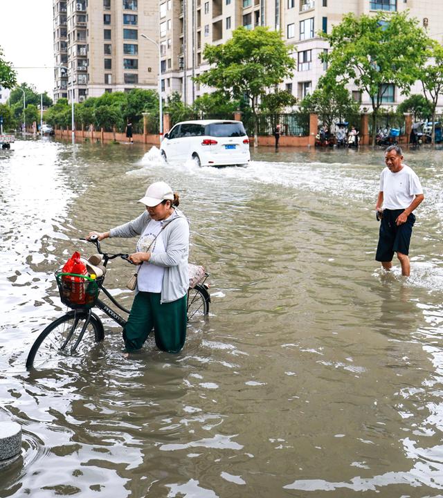 Anwohner versuchen am 12.07.2026 in der Stadt Yueqing, in der ostchinesischen Provinz Zhejiang, eine überflutete Straße nach dem Taifun "Bavi" zu überqueren.