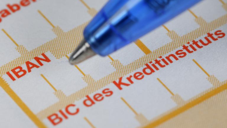 Ein Kugelschreiber liegt neben einem Überweisungsträger mit den Schriftzügen IBAN und BIC.