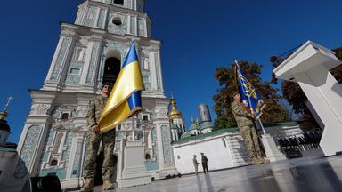 Soldat trägt ukrainische Flagge vor einer Kathedrale in Kiew. Bild von Bodenhöhe nach oben aufgenommen.