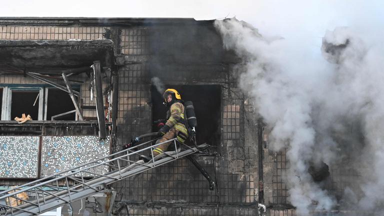 Ukraine, Charkiw: Ein Feuerwehrmann sitzt auf einer ausgefahrenen Leiter, vor einem beschädigten Haus.
