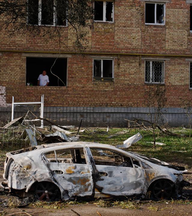Ein Mann blickt am frühen Dienstag nach einem russischen Raketen- und Drohnenangriff in Kiew, Ukraine, aus seiner Wohnung. Das Wohnhaus und ein Auto sind stark beschädigt.