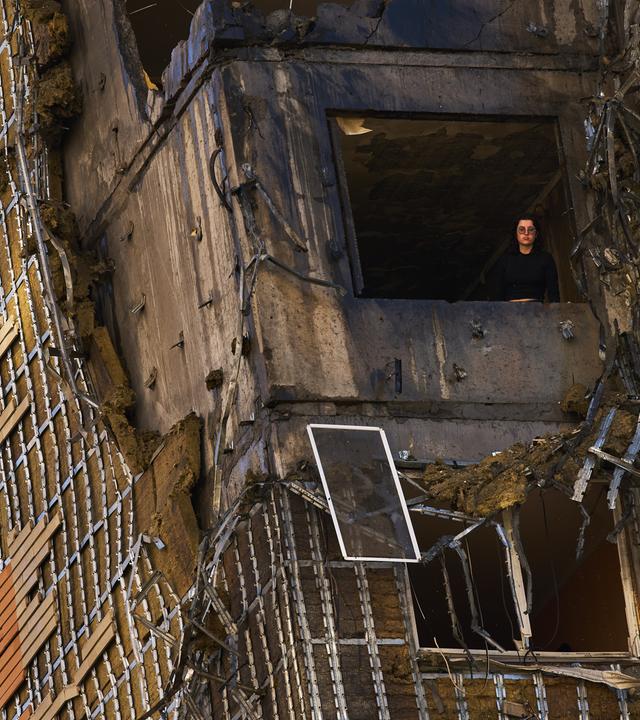 Eine Frau blickt nach einem russischen Drohnenangriff aus einem Fenster eines teilweise beschädigten Wohnhauses