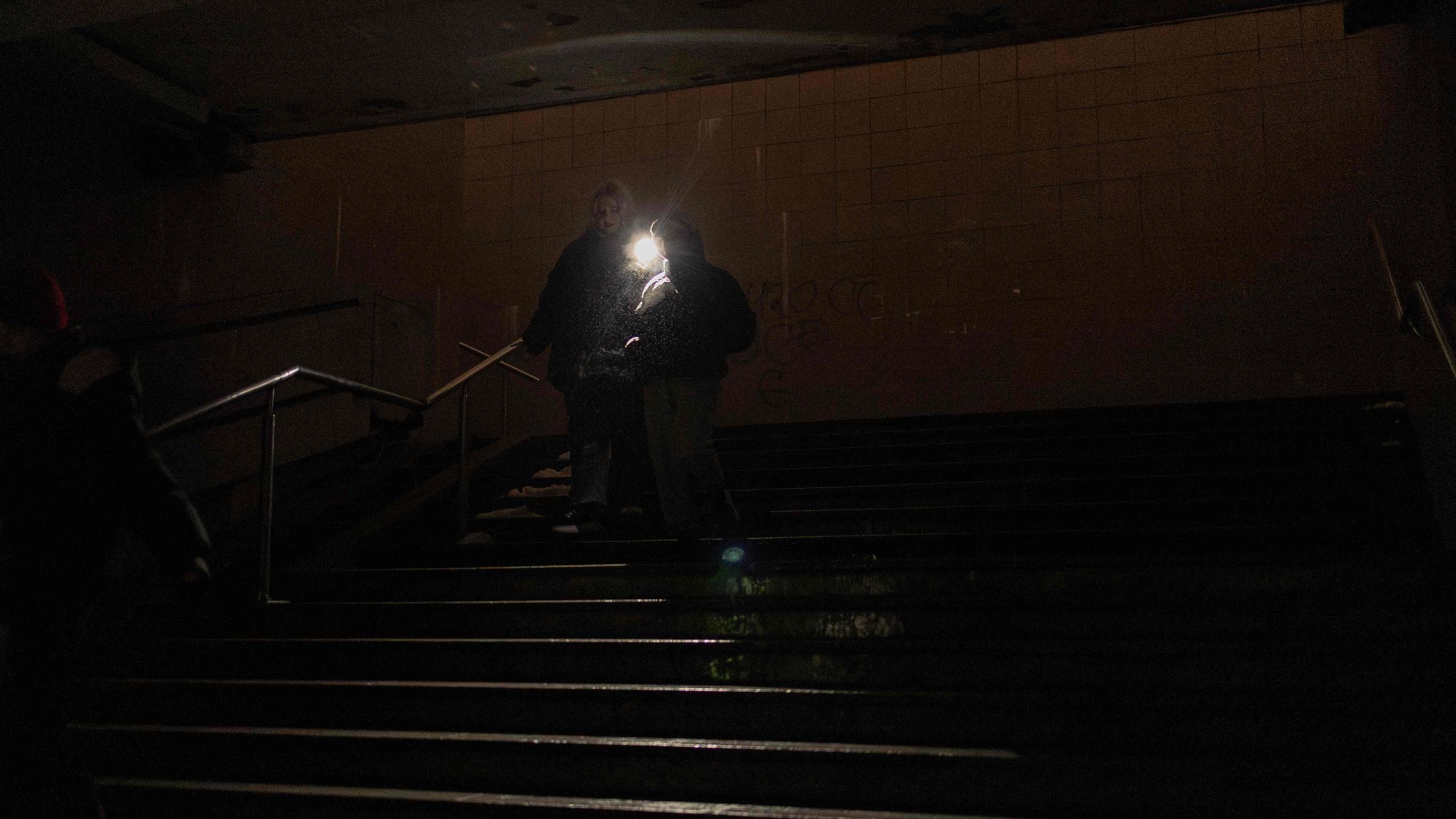 Menschen gehen mit Taschenlampe durch einen dunklen Untergrundgang in Kiew während eines Stromausfalls.