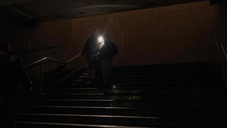 Menschen gehen mit Taschenlampe durch einen dunklen Untergrundgang in Kiew während eines Stromausfalls.