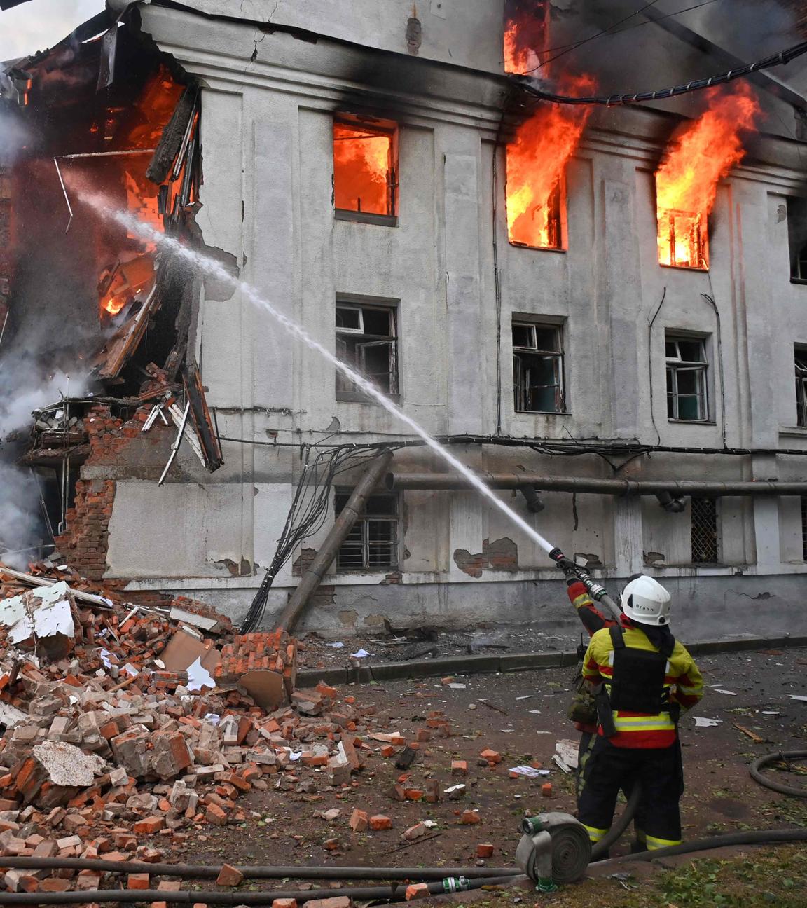 Einen kniender Feuerwehrmann löscht ein brennendes ziviles Gebäude in Charkiw in der Ukraine.
