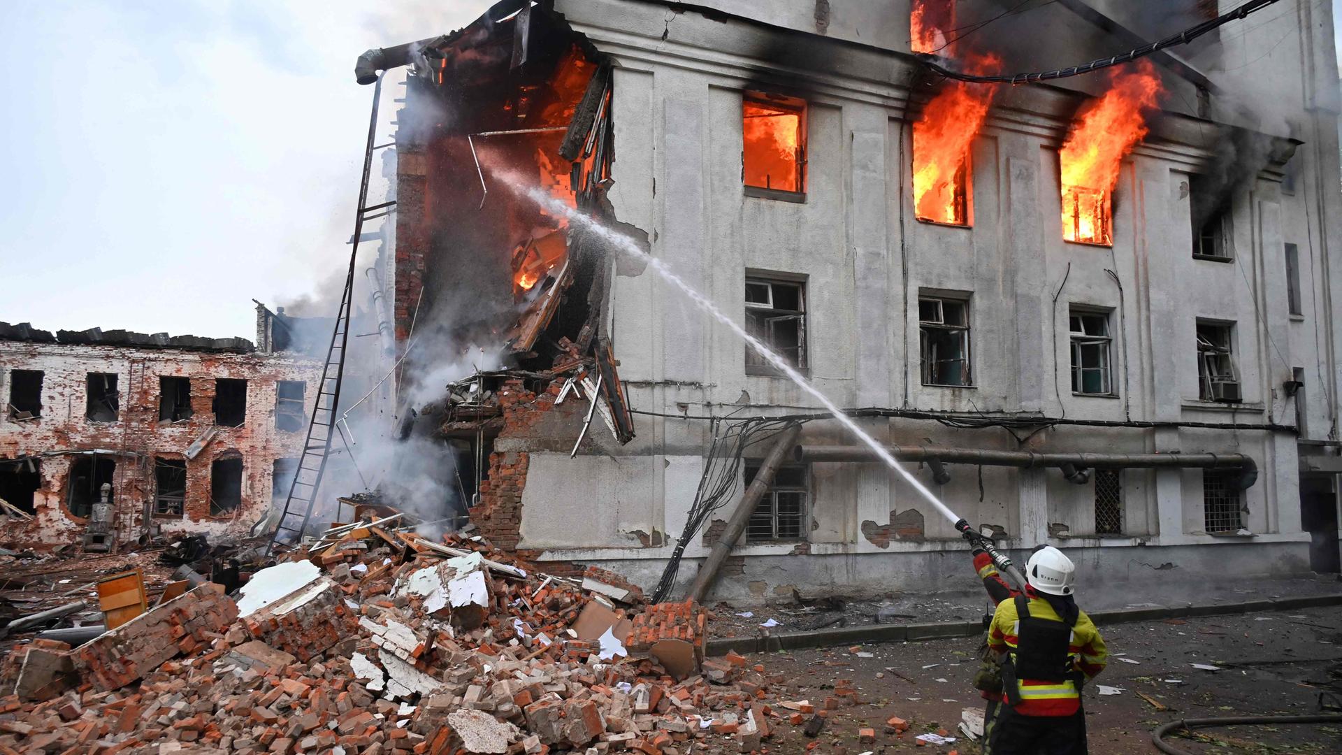 Einen kniender Feuerwehrmann löscht ein brennendes ziviles Gebäude in Charkiw in der Ukraine.