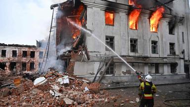 Einen kniender Feuerwehrmann löscht ein brennendes ziviles Gebäude in Charkiw in der Ukraine.