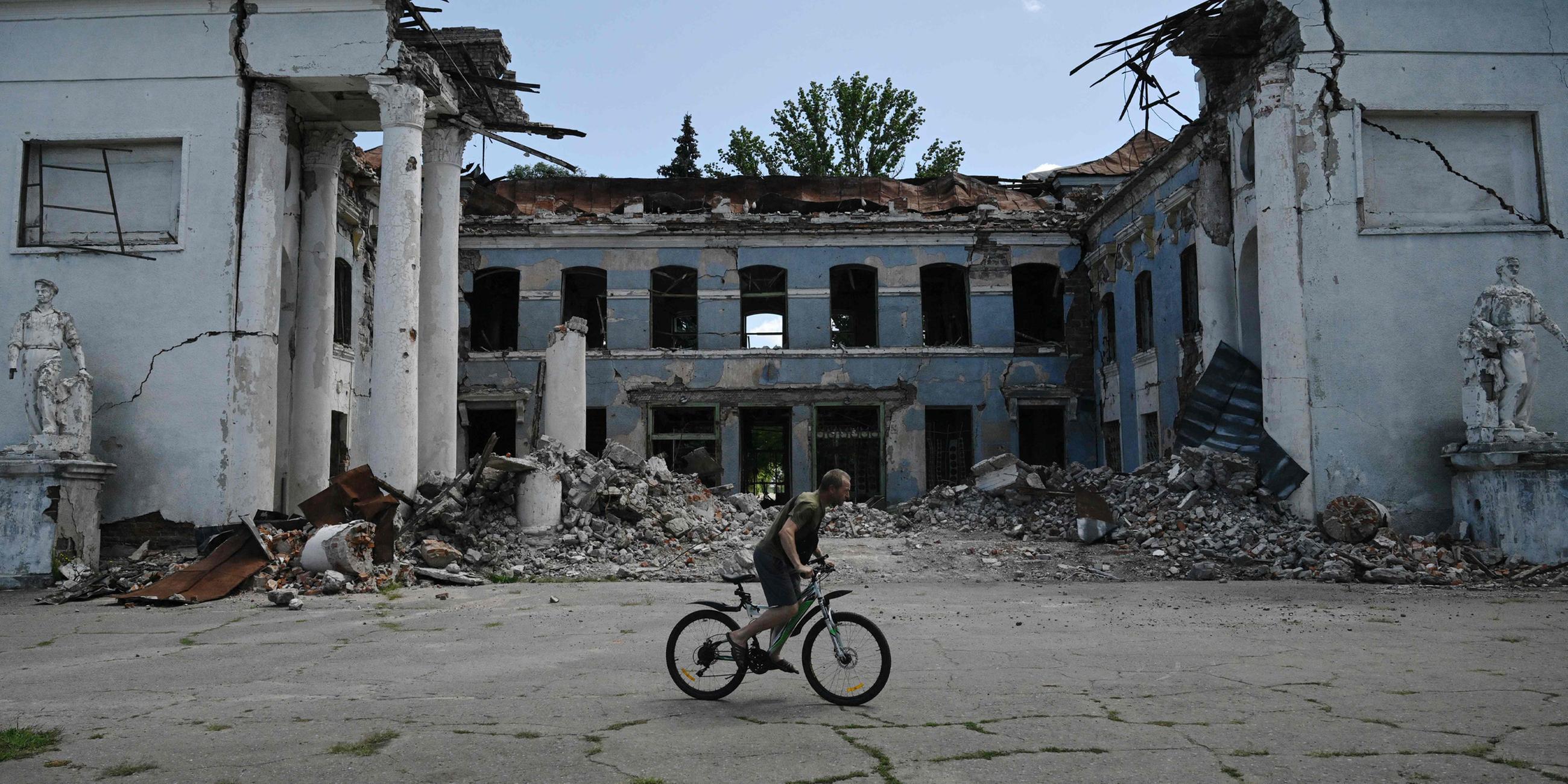 Ein Mann fährt mit dem Fahrrad an einem zerstörten Gebäude in Druzhkivka, Region Donezk, vorbei – aufgenommen am 15. August 2025.