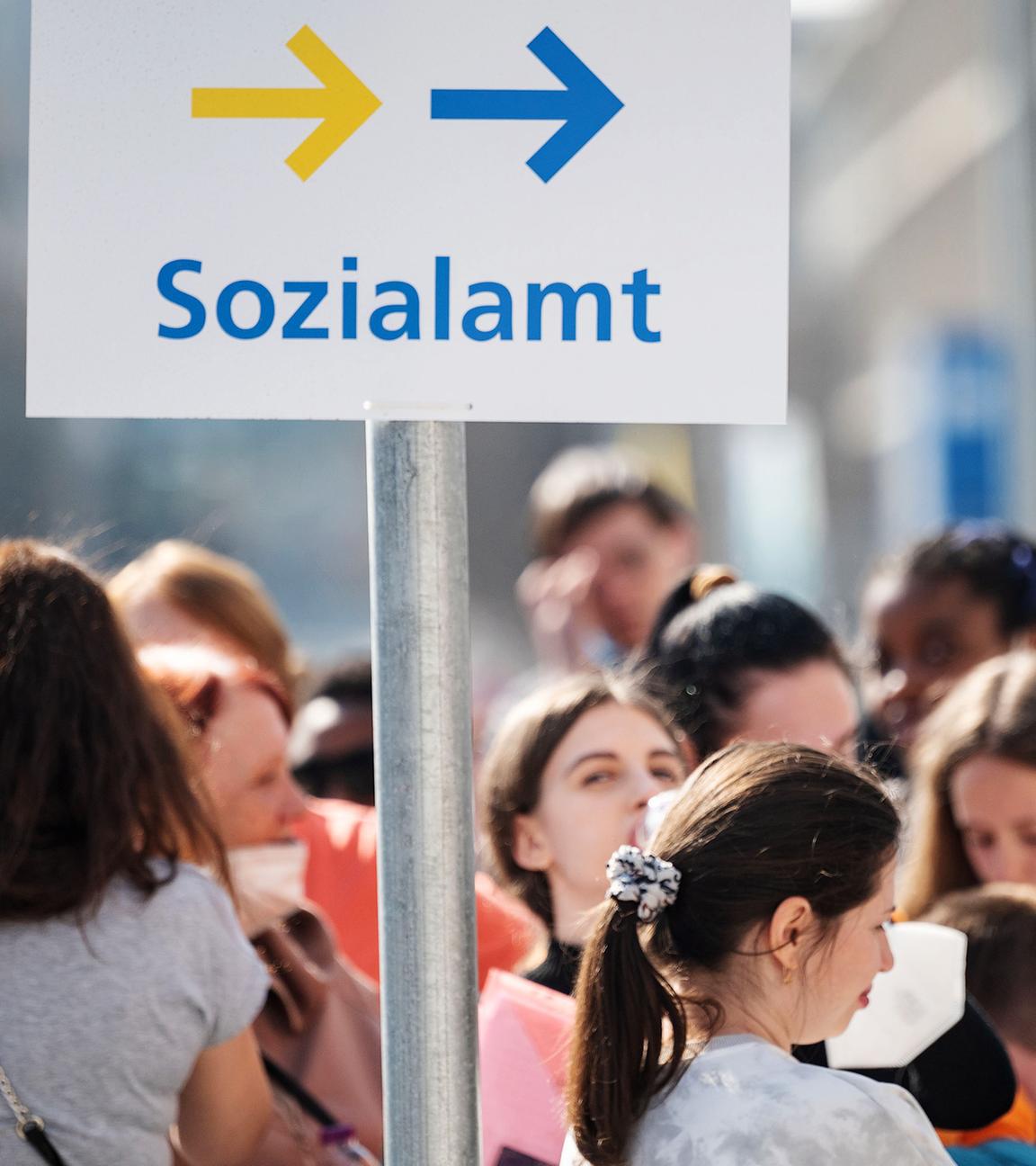 Flüchtlinge, darunter der größte Teil aus der Ukraine, und eine Helferin (r) stehen vor einer Außenstelle des Sachgebiets Flüchtlinge der Ausländerbehörden und der Abteilung Flüchtlinge des Sozialamts in der Innenstadt in einer Schlange
