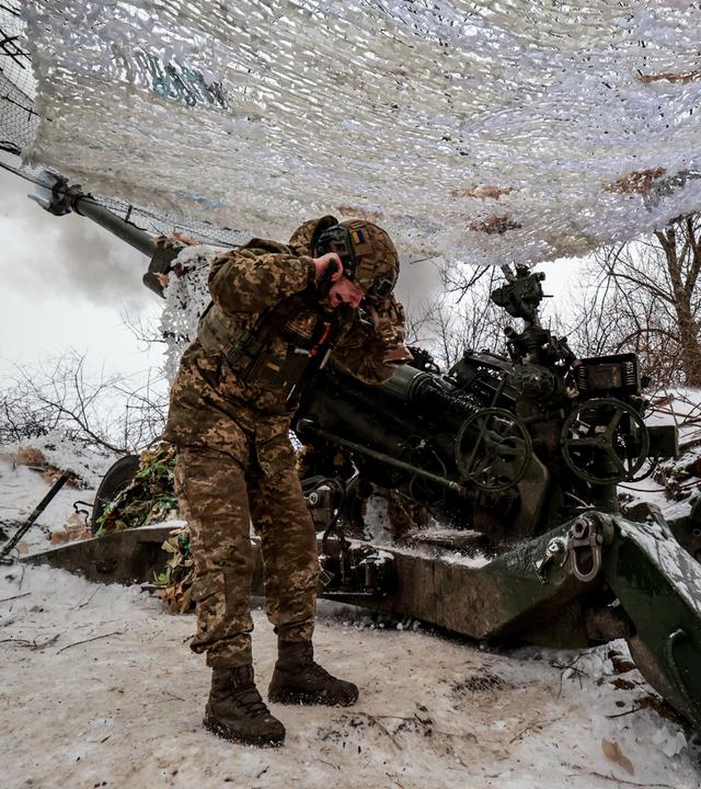 Ein Soldat hält sich vor Kriegsgerät die Ohren zu.