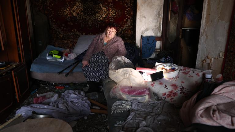 Eine ältere Frau sitzt in ihrer beschädigten Wohnung, nachdem eine russische Drohne das Wohnhaus getroffen hat.
