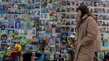 Eine Frau mit Blumen in der Hand gedenkt am 24. Februar 2026 an der Gedenkmauer den Gefallenen der Ukraine in Kiew, während die Ukraine den vierten Jahrestag des russischen Einmarsches erinnert.