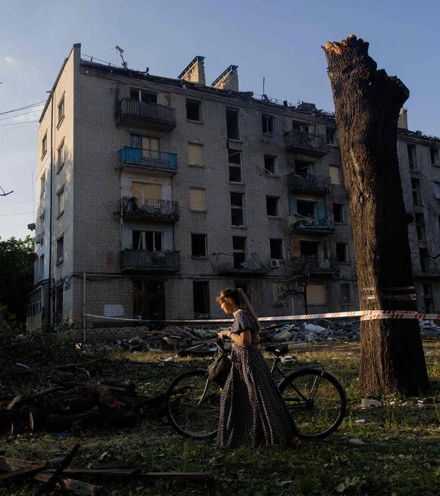 Eine Frau mit einem Fahrrad geht an einem Wohngebäude vorbei, das nach einem russischen Luftangriff auf die ukrainische Hauptstadt Kiew am 2. Juli 2026 – inmitten der russischen Invasion in der Ukraine – beschädigt wurde.