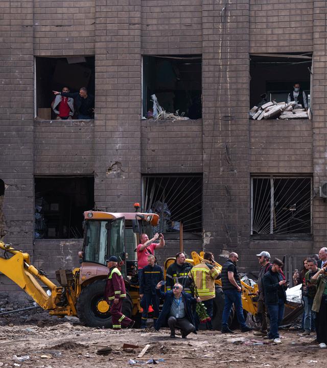 15.05.2026, Ukraine, Kiew: Menschen schauen durch die Fenster eines beschädigten Gebäudes nach einem russischen Angriff auf ein Wohnviertel.