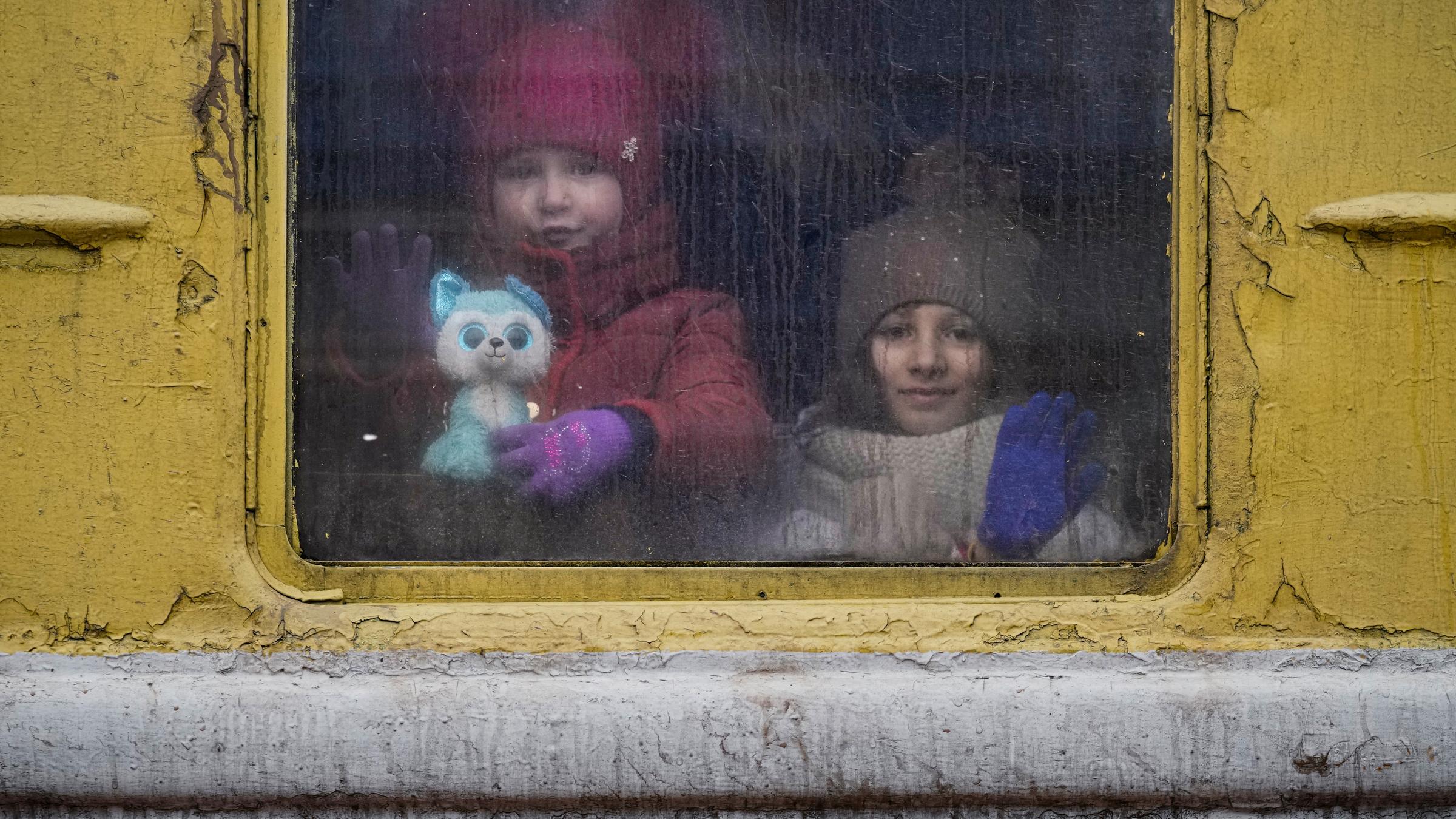 Kinder aus dem Fenster eines Zuges, sind warm angezogen mit Mütze und Winterjacke