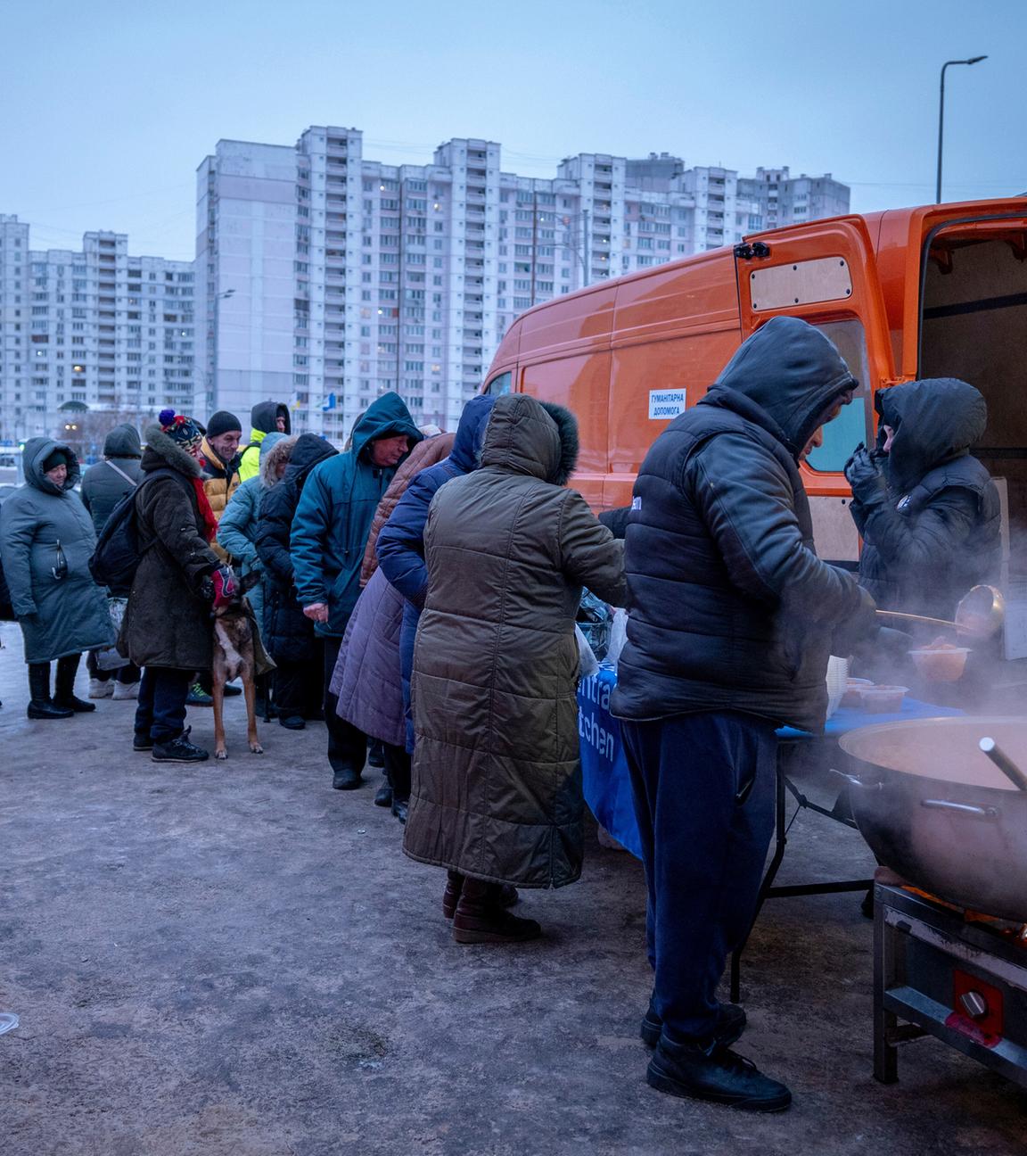 Menschen, die nach den russischen Luftangriffen ohne Strom sind, warten in einem Wohnviertel in Kiew auf kostenlose warme Mahlzeiten.