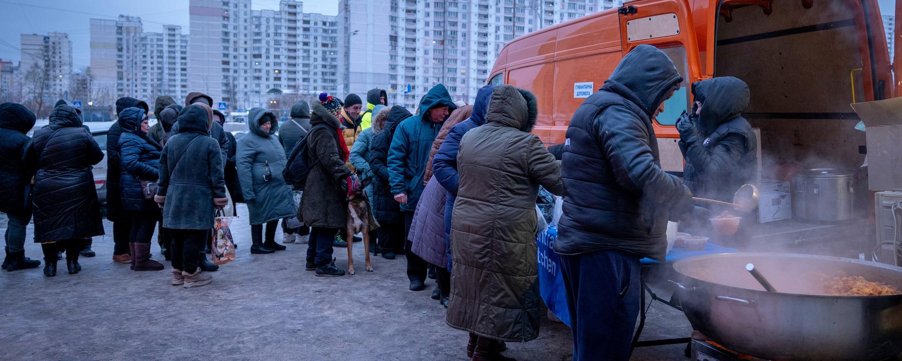 Menschen, die nach den russischen Luftangriffen ohne Strom sind, warten in einem Wohnviertel in Kiew auf kostenlose warme Mahlzeiten.