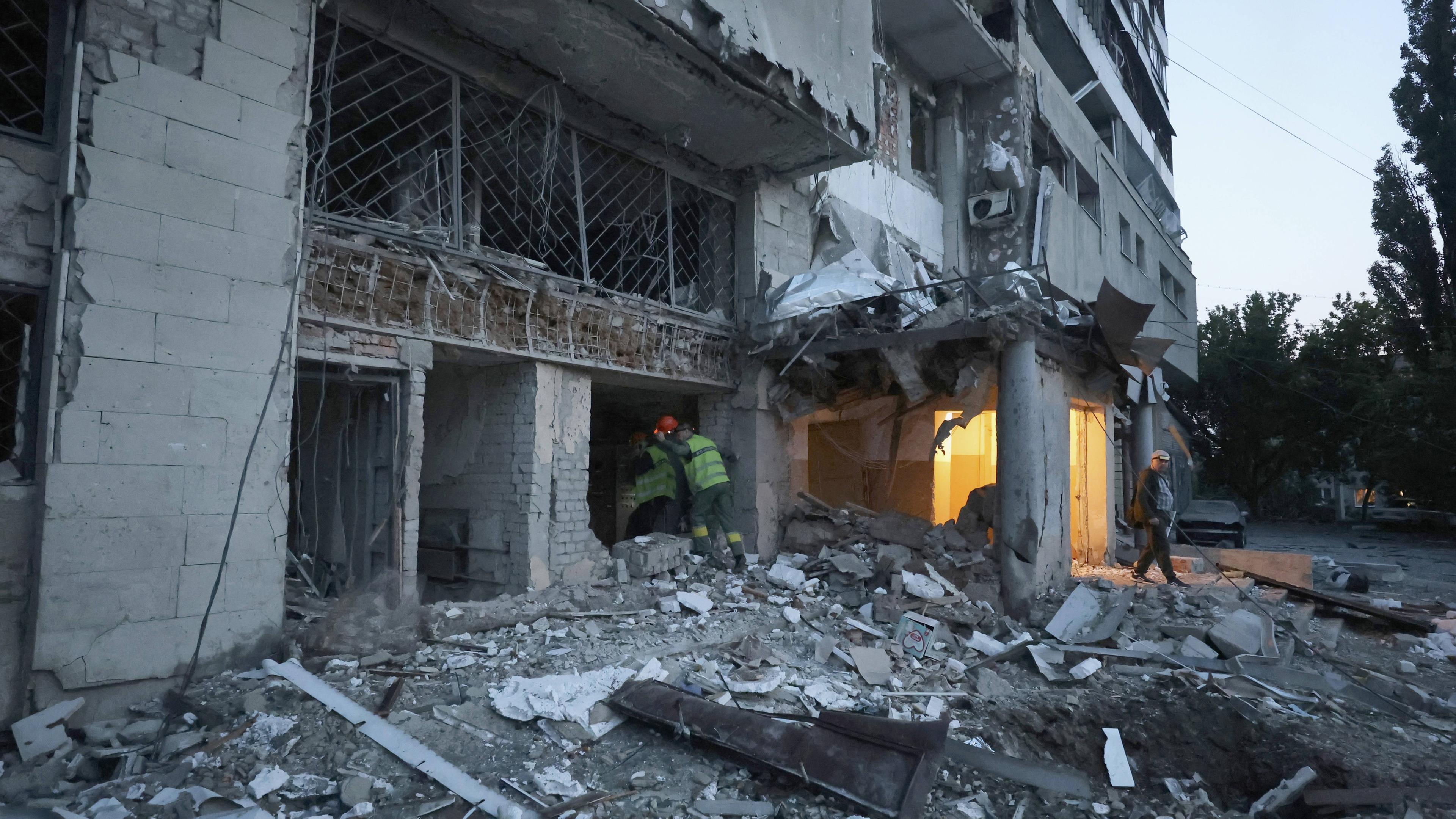 Städtische Angestellten betreten einen zerstörten Wohnblock in Charkiw.
