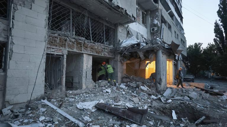 Städtische Angestellten betreten einen zerstörten Wohnblock in Charkiw.