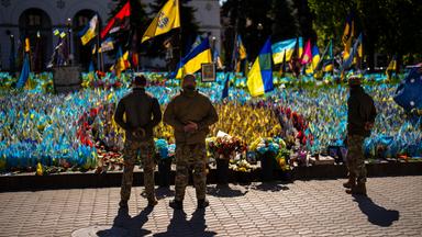 Ukrainian service men stand next to Ukrainian flags and photographs placed in memory of civilians and soldiers killed during the war, at the Independence square in central Kyiv, Saturday, April 20, 2024. 