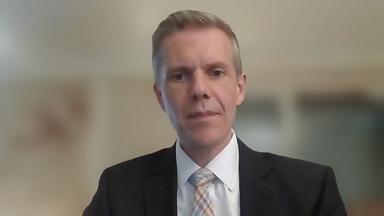 Marcus Keupp sitzt an seinem Schreibtisch im Anzug und spricht in die Kamera, der Hintergrund ist verpixelt.