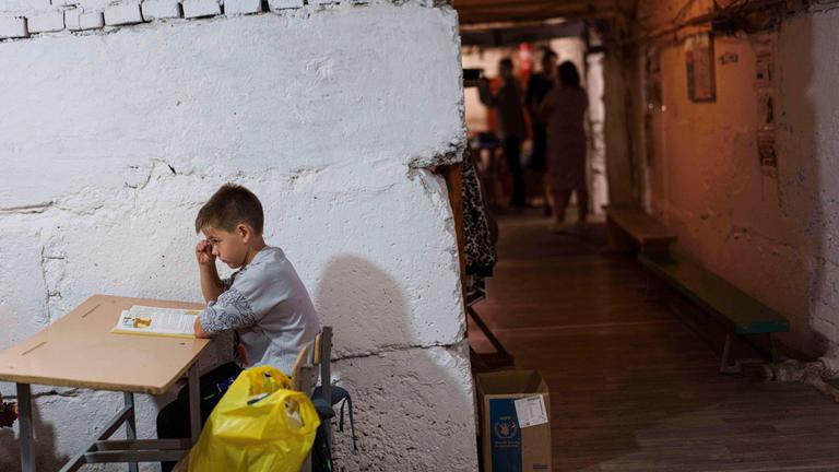 Ukraine, Bobryk Oblast Kiew: Ein Schüler hört einem Lehrer bei einer Unterrichtsstunde im Keller eines städtischen Gebäudes während des ersten Schultages zu. 