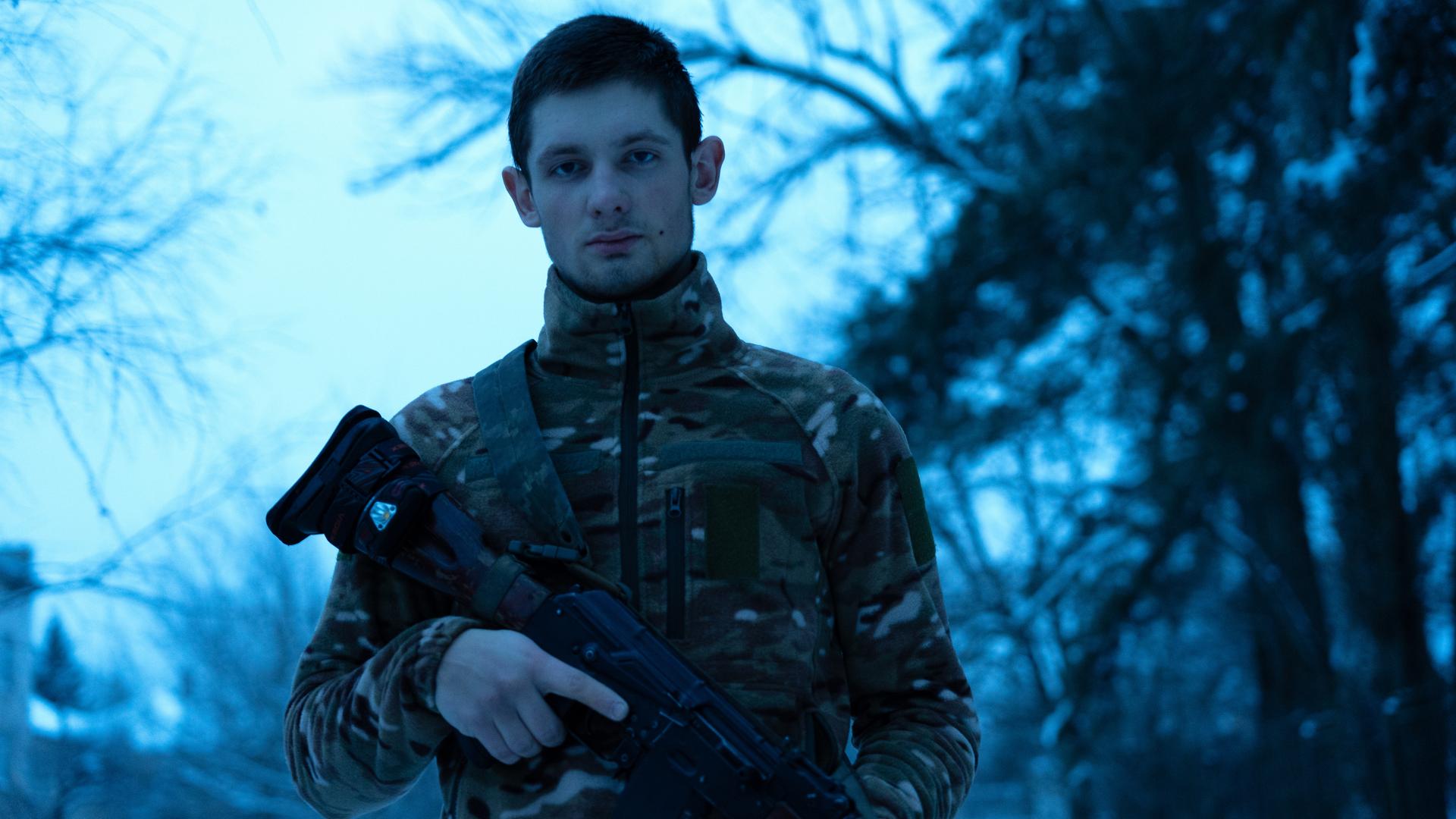 Ein Soldat in Uniform mit Gewehr steht in einem verschneiten Wald.