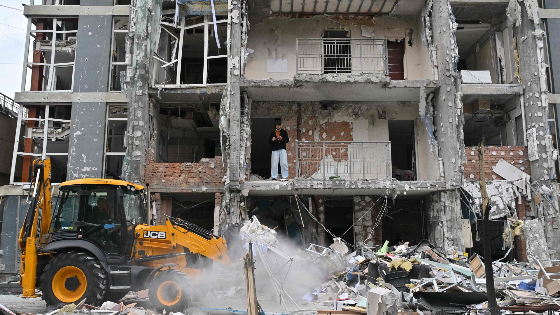 Zerstörte Gebäude nach Luftangriffen. Außerdem ein kleiner Traktor, der für Aufräumarbeiten genutzt wird. In dem zerstörten Gebäude steht ein Mann.