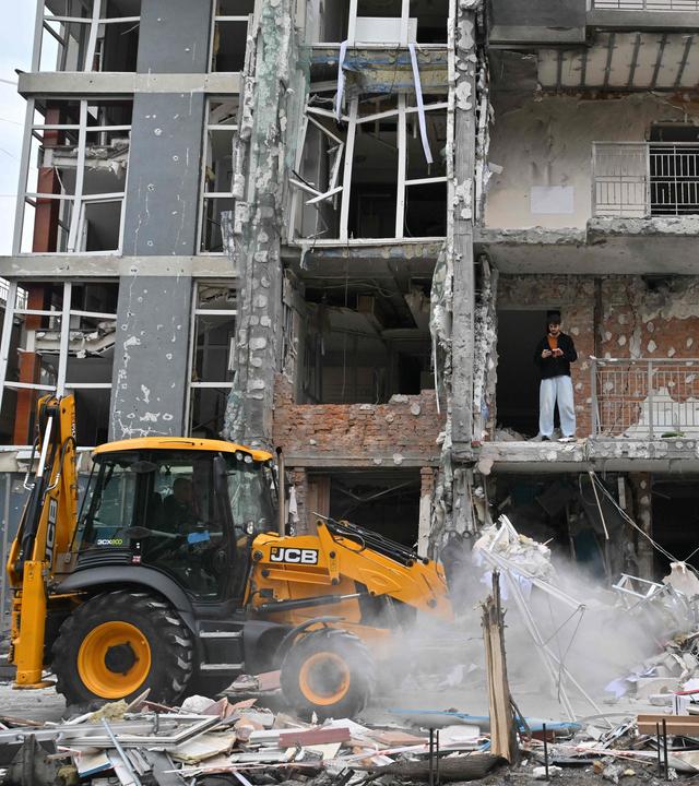 Zerstörte Gebäude nach Luftangriffen. Außerdem ein kleiner Traktor, der für Aufräumarbeiten genutzt wird. In dem zerstörten Gebäude steht ein Mann.