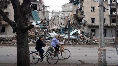 Zwei Personen fahren mit dem Fahrrad an einem beschädigten Gebäude in Slowjansk in der Ukraine vorbei.