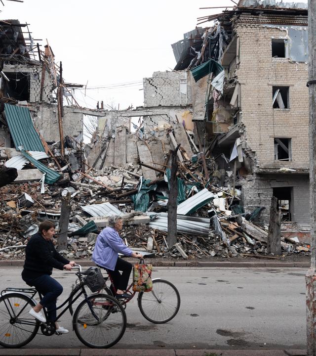 Zwei Personen fahren mit dem Fahrrad an einem beschädigten Gebäude in Slowjansk in der Ukraine vorbei.
