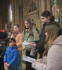 Ein Geistlicher übergibt einer Gruppe von fünf Kindern etwas in einer Kirche.